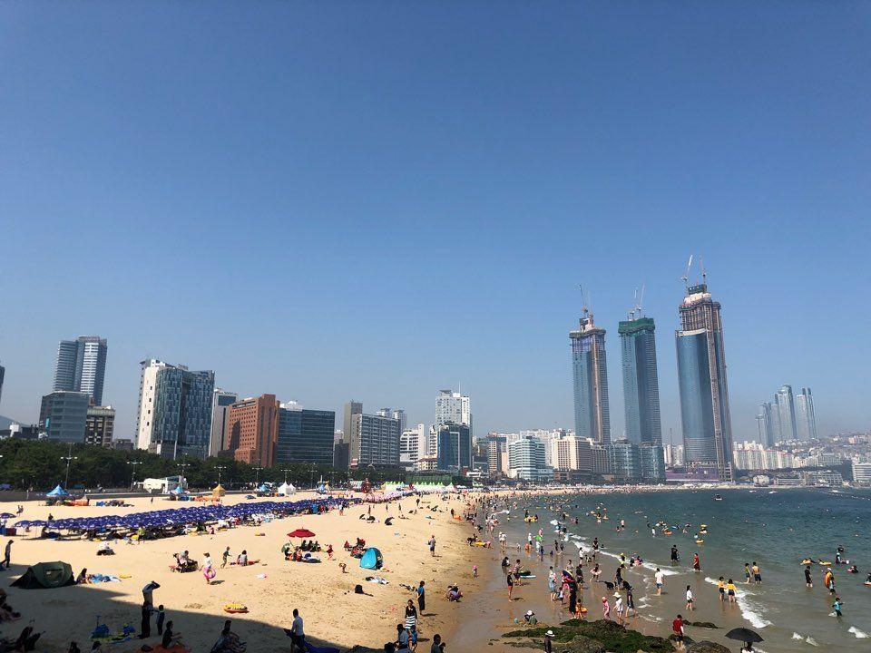 Busy Haeundae Beach in Busan, filled with tourists enjoying the sea and sand under clear skies.